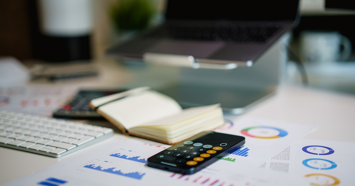 Laptop, financial charts, and smartphone calculator on an office desk